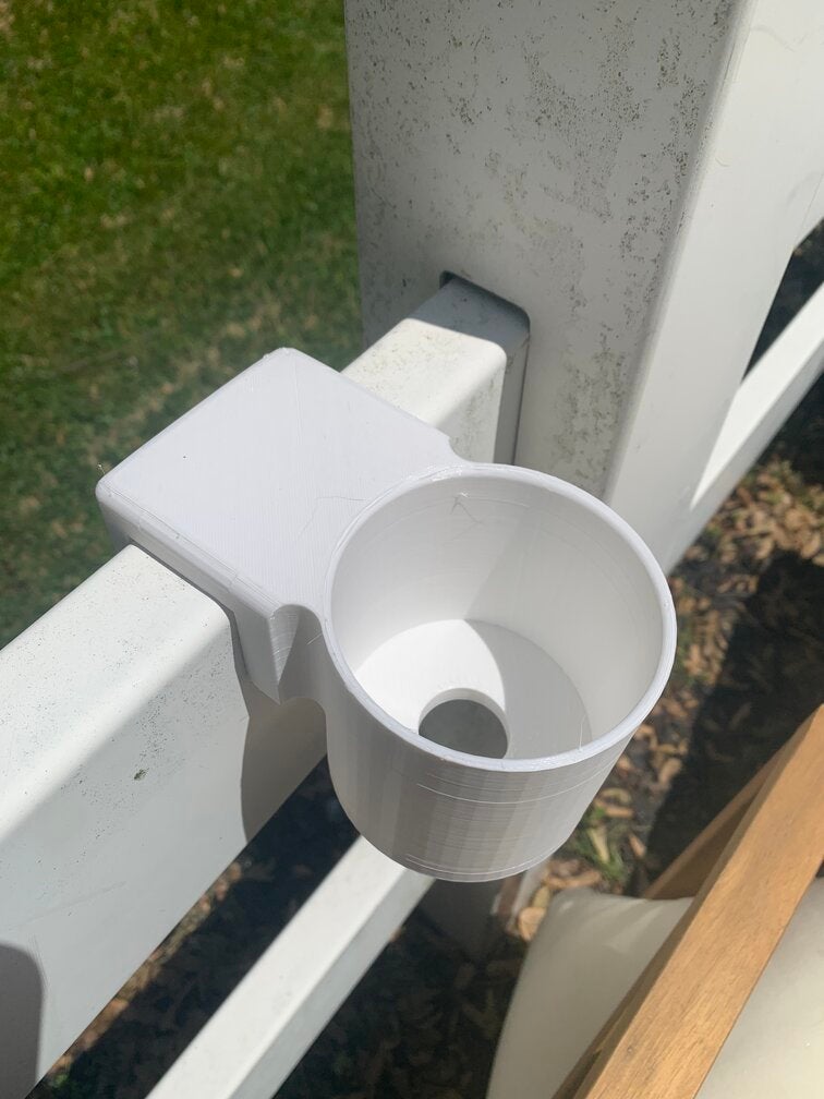 A photo of the 3D printed cup holder mounted to the fence.